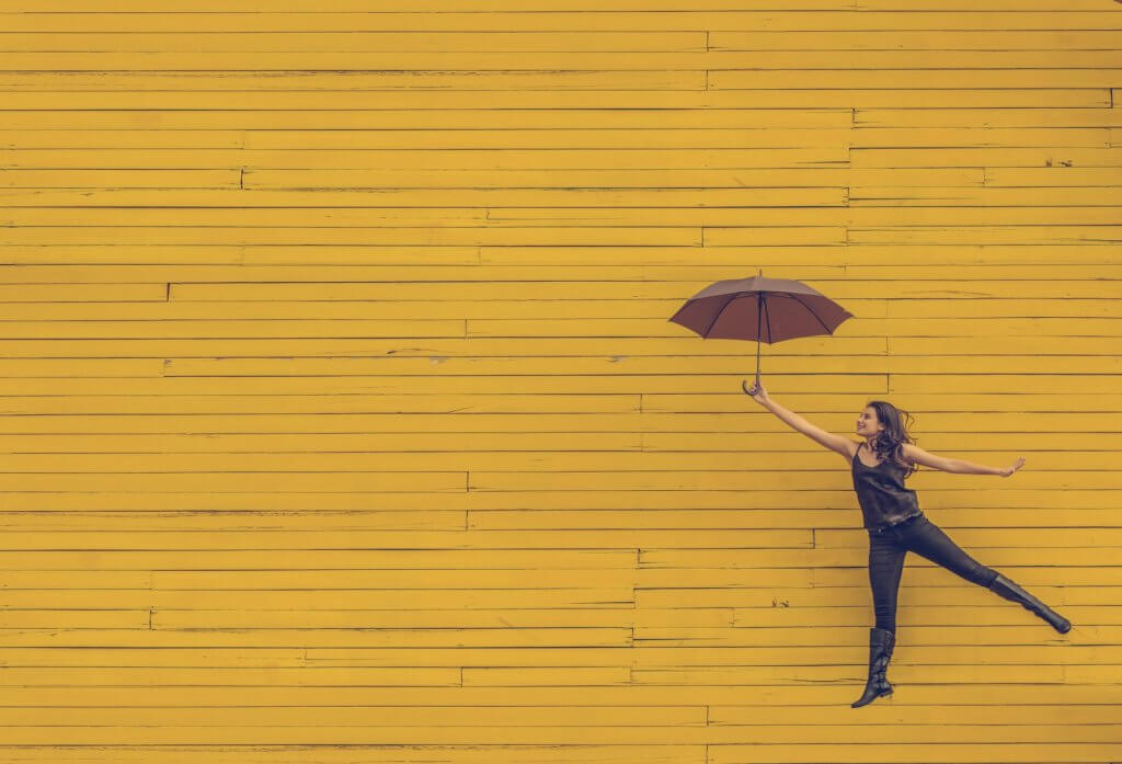 women with umbrella in front of yellow wall