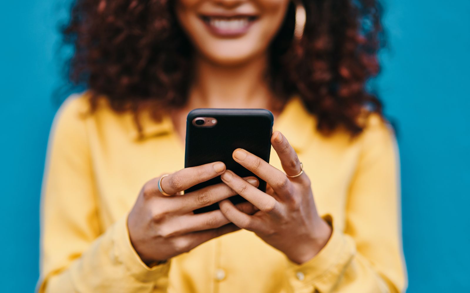 Happy woman smiling while looking at her phone, possibly engaging with a loyalty app or social media.