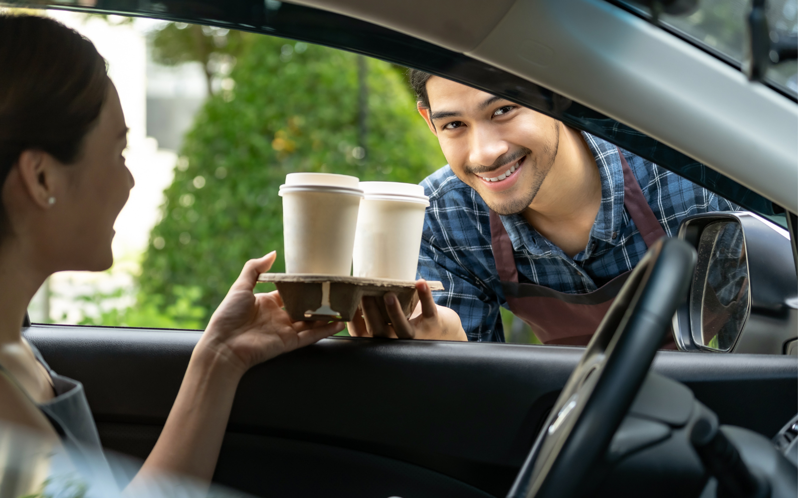 Man holding takeaway coffees and handing them to a woman in a car. 