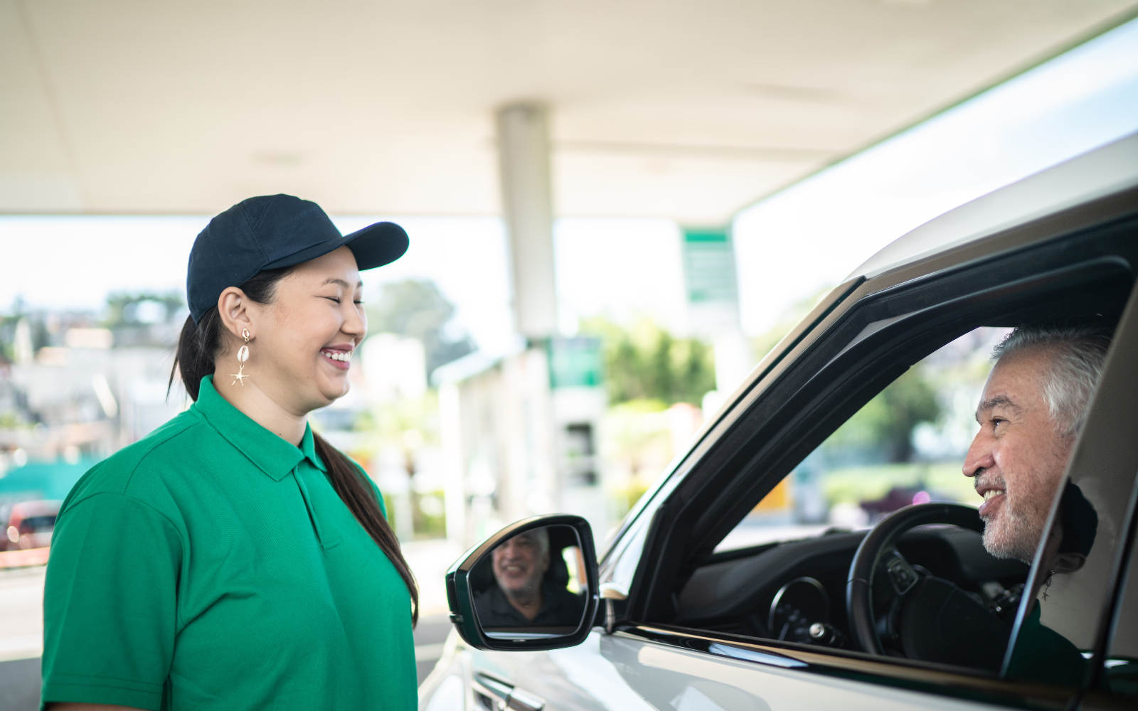 Gas station attendant smiling at a customer in a car. 