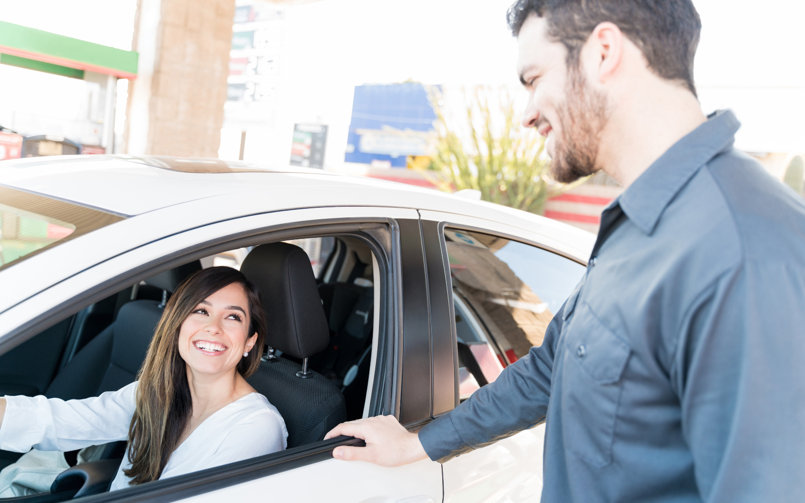 A man smiling at a woman customer in a car. 