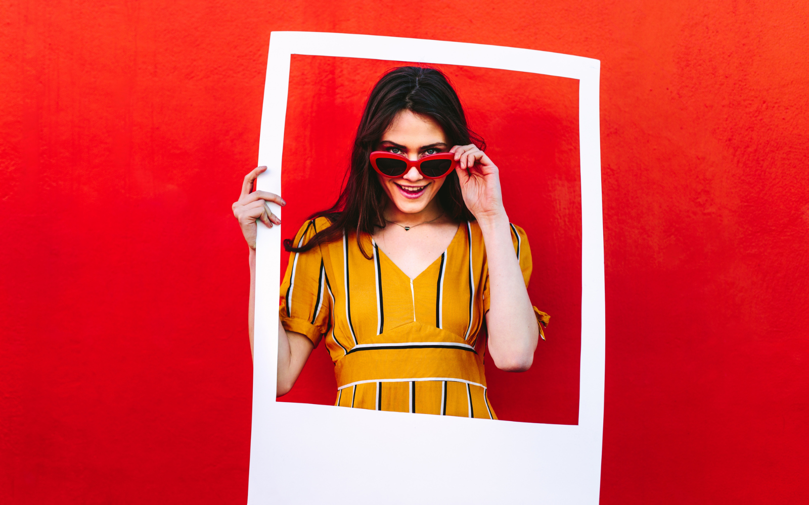 A woman in front of a red background smiling and holding a social media photo frame. 