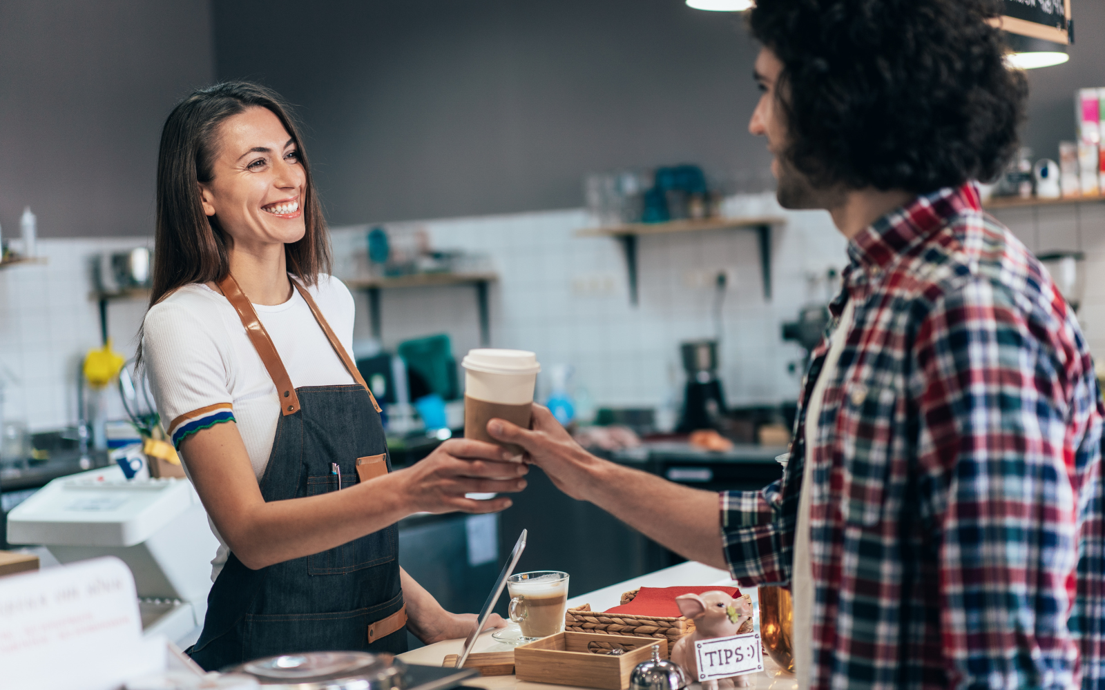 A barista smiling and handing a customer their coffee